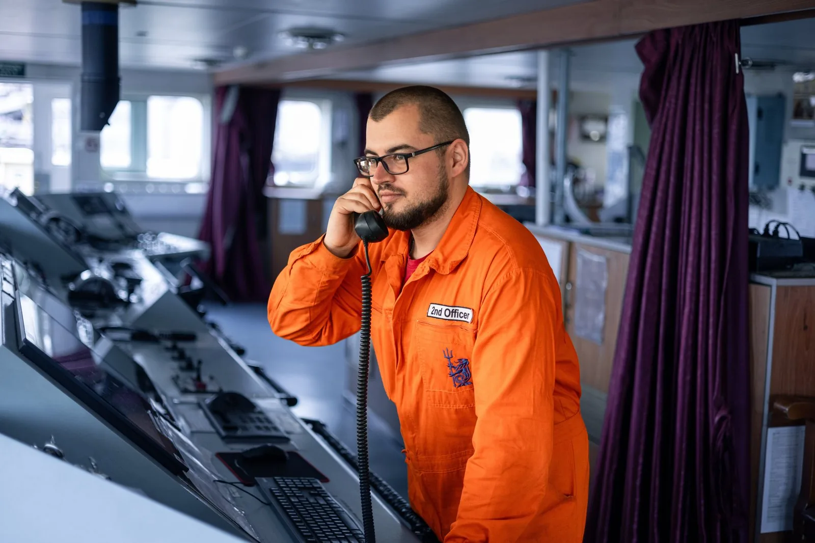 A 2nd Officer on the ship's bridge coordinating with shore-side commercial management by phone — integration of operational and commercial decision-making.
